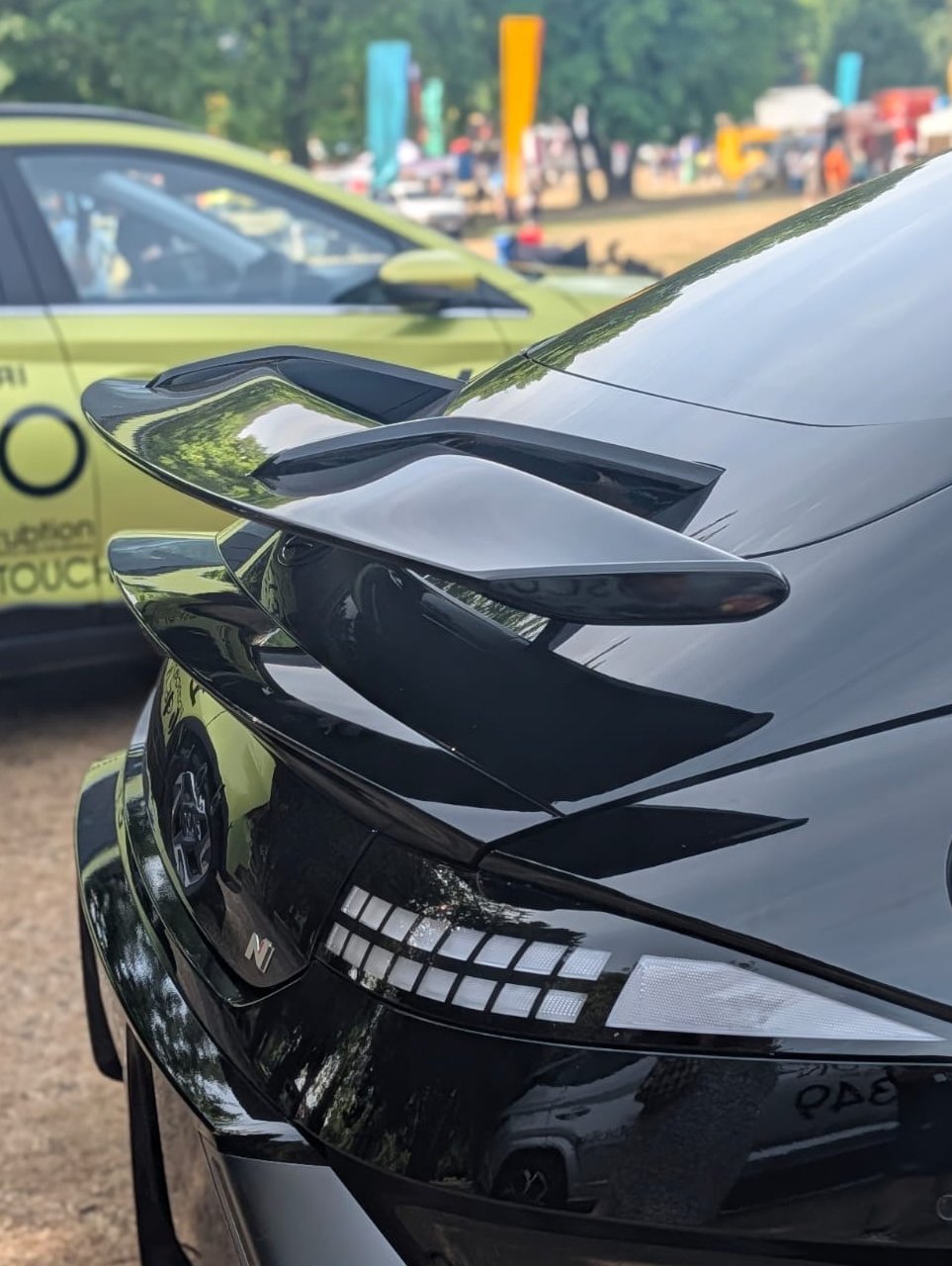 Close-up of a black car's rear with a spoiler, parked beside a lime green vehicle.