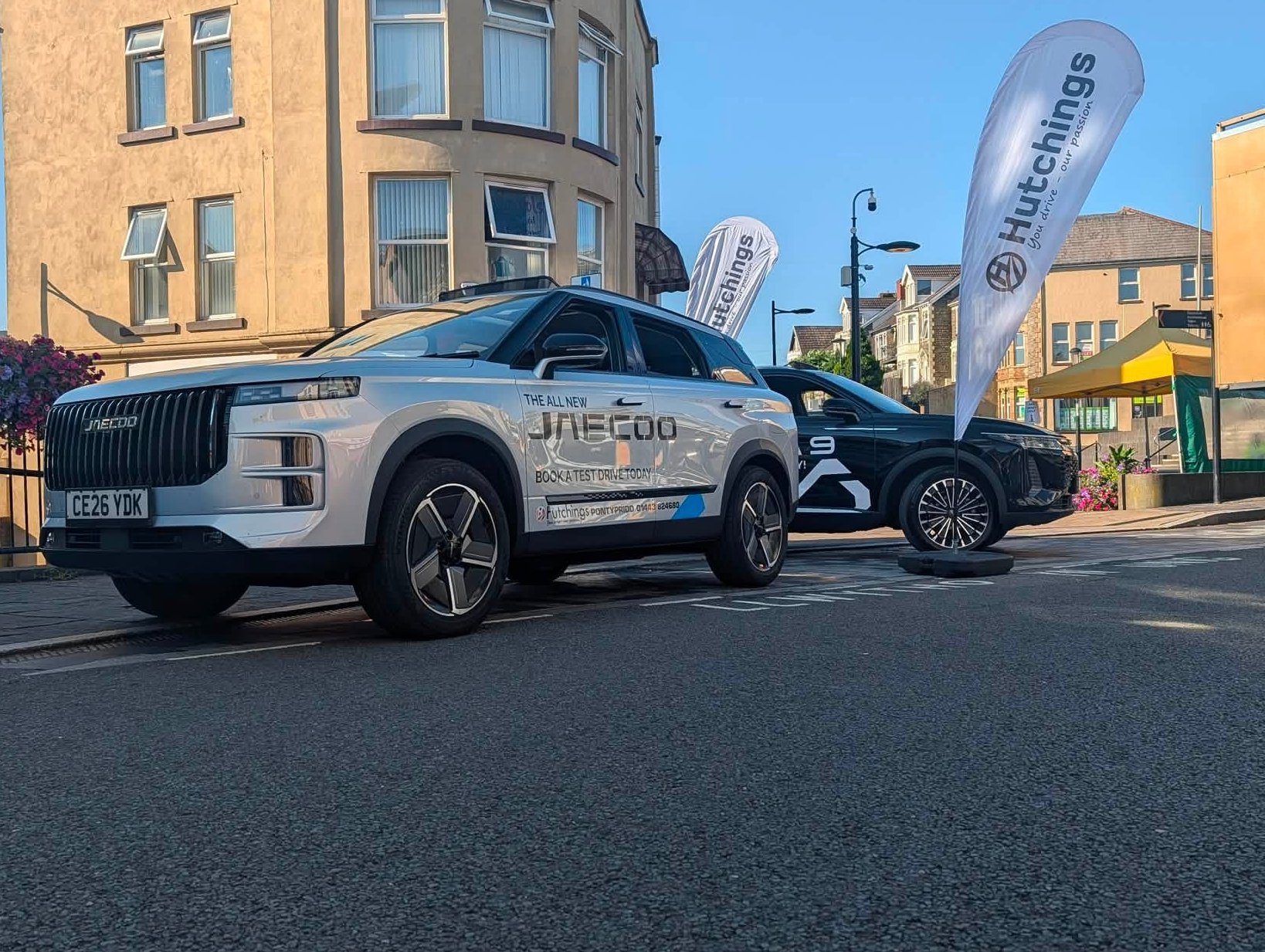 Two cars parked on a street, with branded flags beside them.