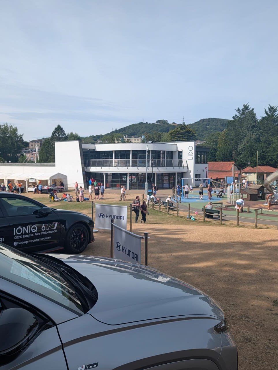 Cars parked near a public park with a lido building in the background.