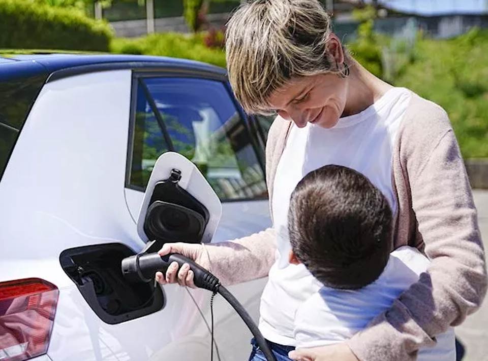 Woman charging an electric car while holding a child.