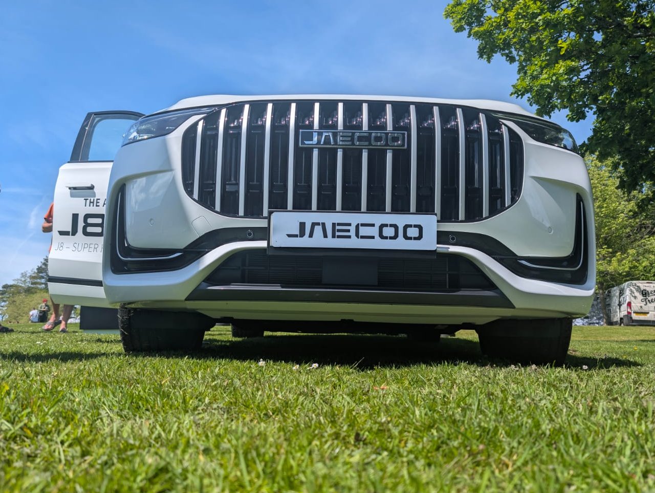 Front view of a Jaecoo car on grass with two people in the background.