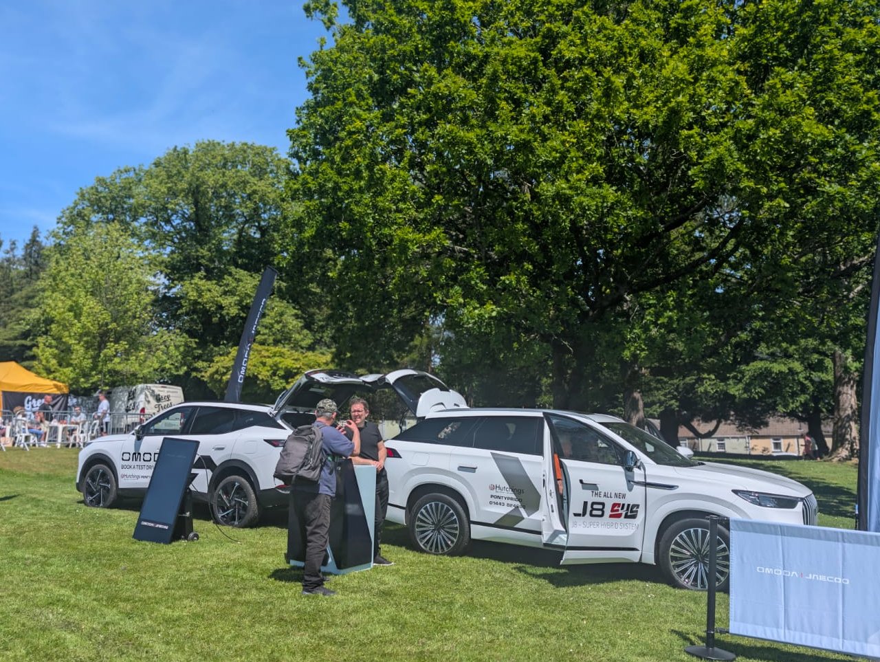 Two white cars on display outdoors with people examining them.