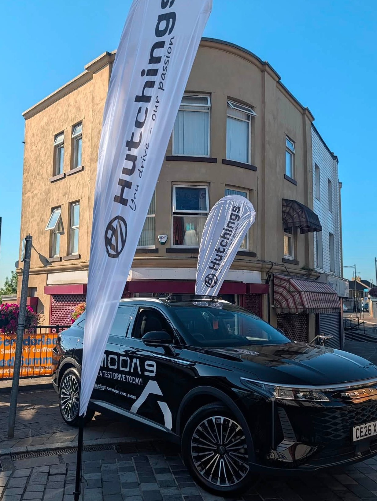 Black car on display wOJ BARGOED ith Hutchings branding flags in front of a building.
