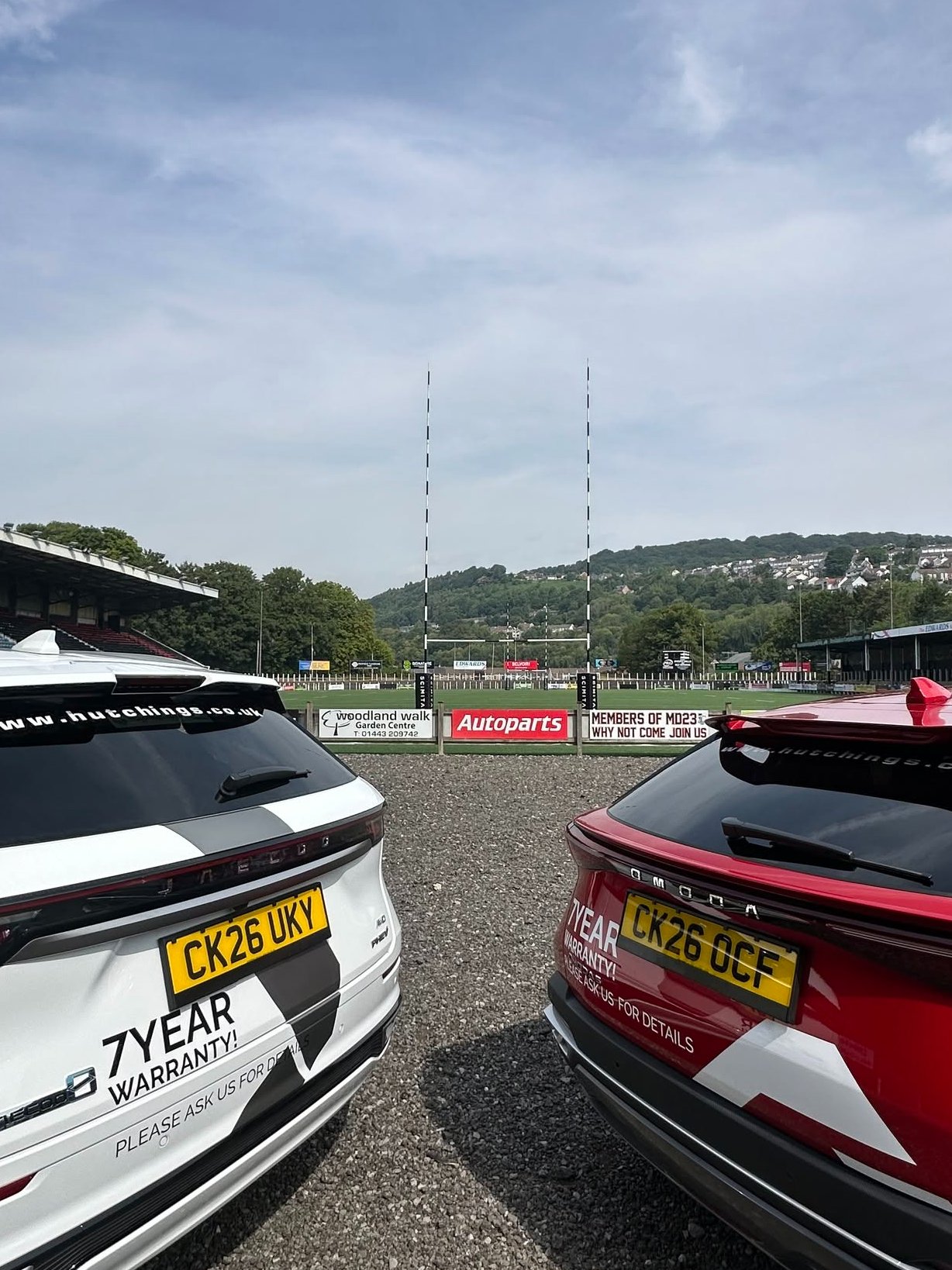 Two modern cars parked with a rugby pitch and goalposts in the background.