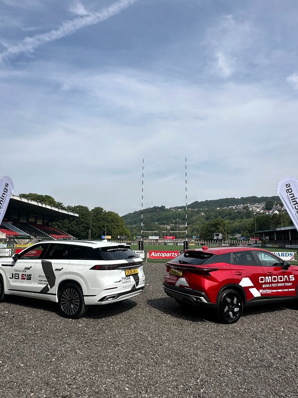Two cars parked on a gravel surface with banners beside them.
