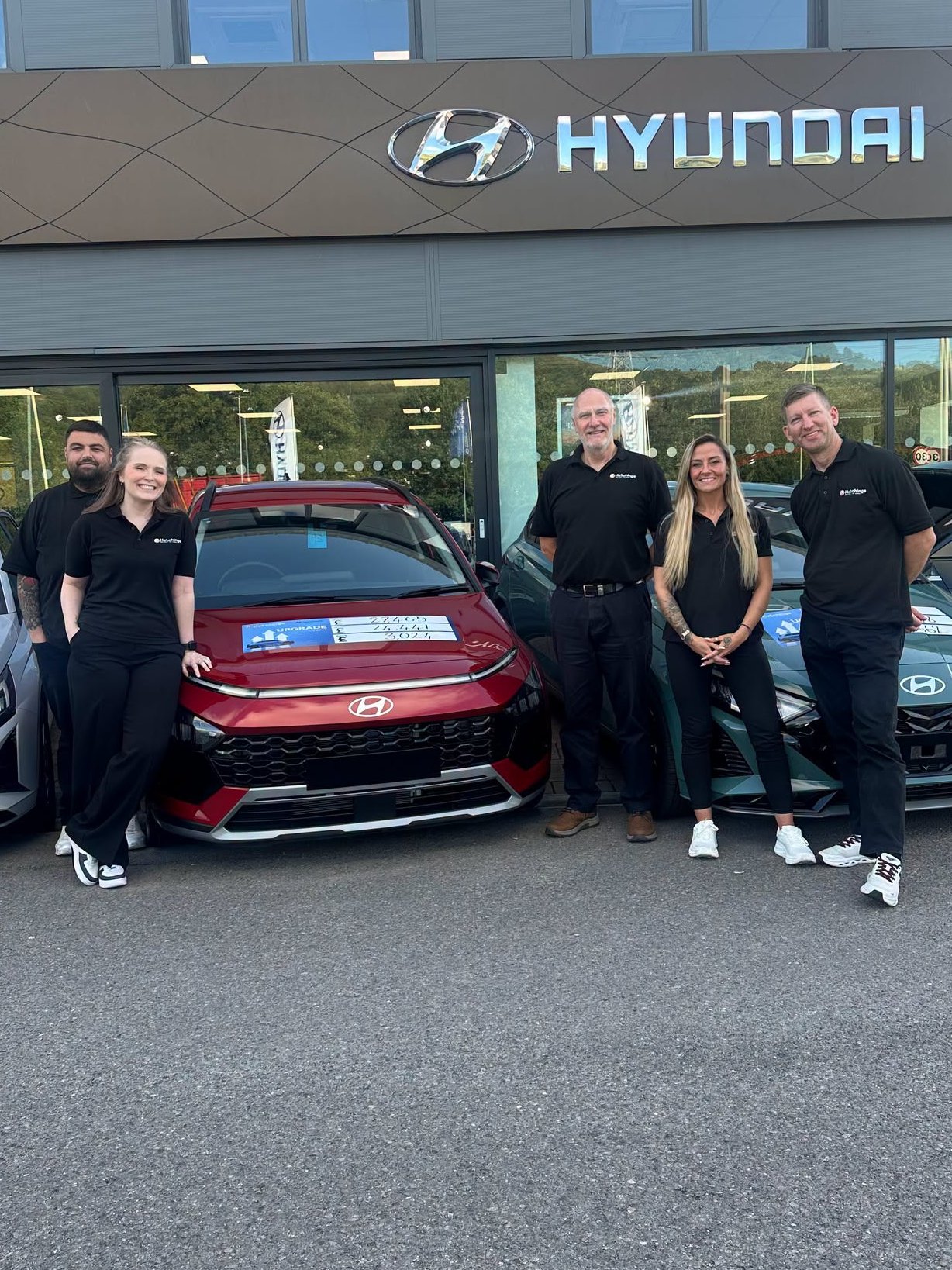 Five people standing in front of Hyundai cars at a dealership.