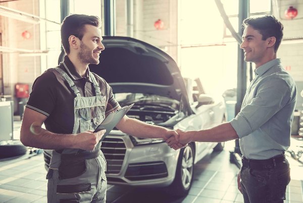 two men shaking hands in front of a car